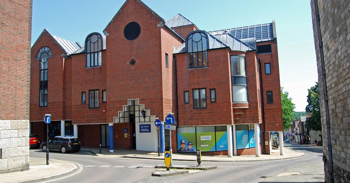 Hampshire Constabulary's Operational Headquarters, a red-brick building on a street corner in Winchester, with police signage and a wall-mounted banner at street level.