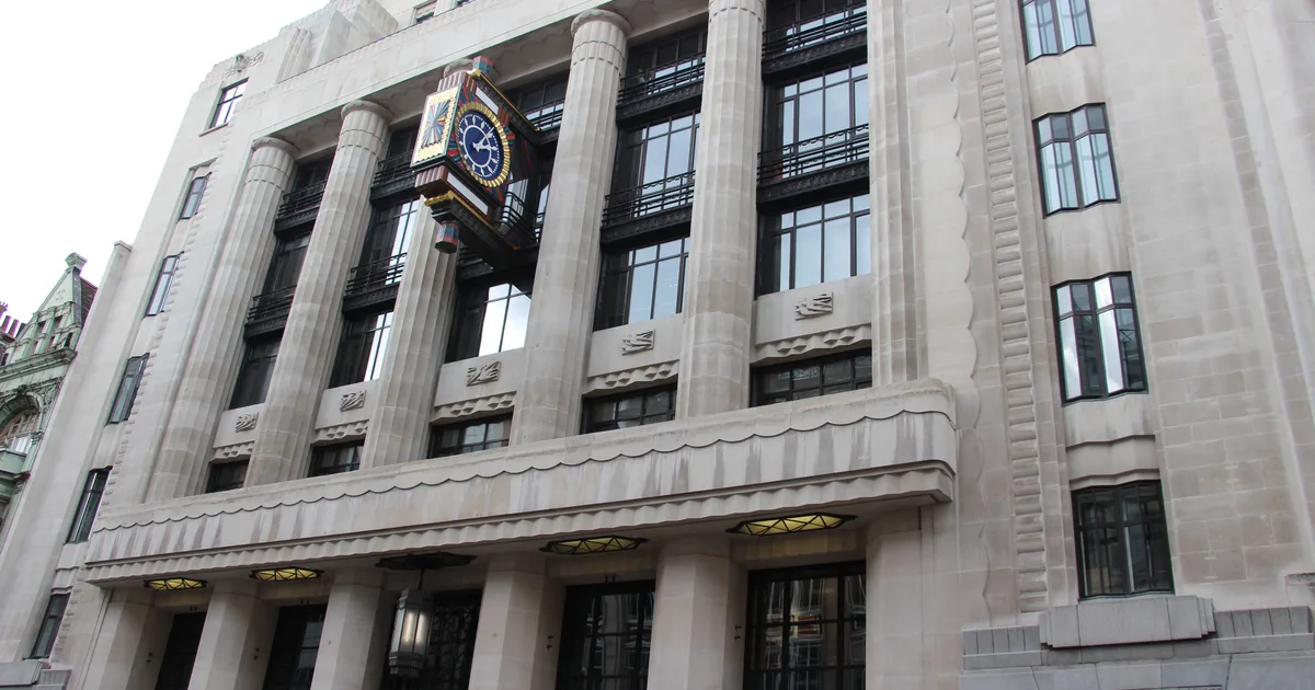 Low-angle view of the former Daily Telegraph Building on Fleet Street, London, showing its Art Deco stone columns and an ornate clock mounted on the facade.