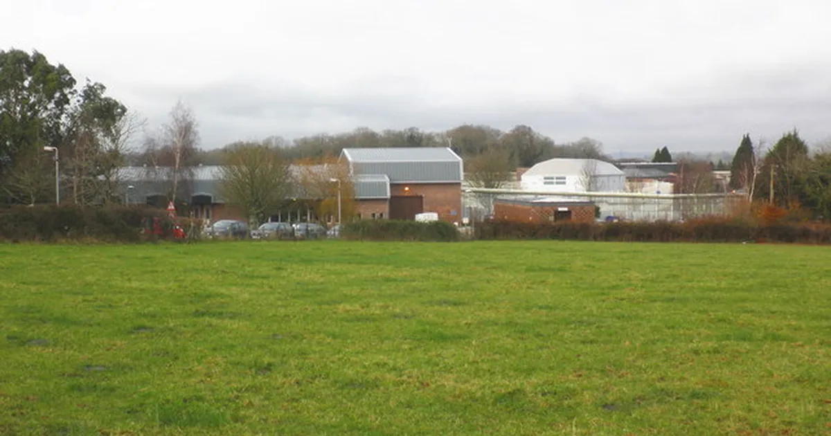 A red-brick prison building behind a high perimeter fence, HM Prison Channings Wood, Devon.