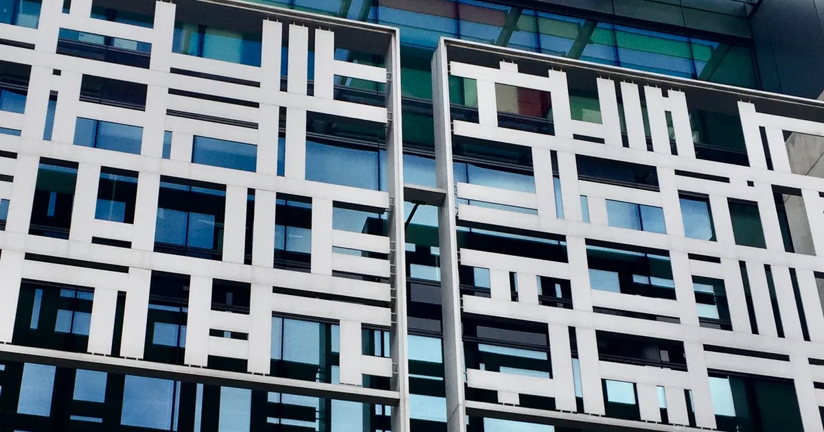 Looking up at the white geometric lattice facade of the Home Office building at 2 Marsham Street, London, with a colourful glass canopy above.