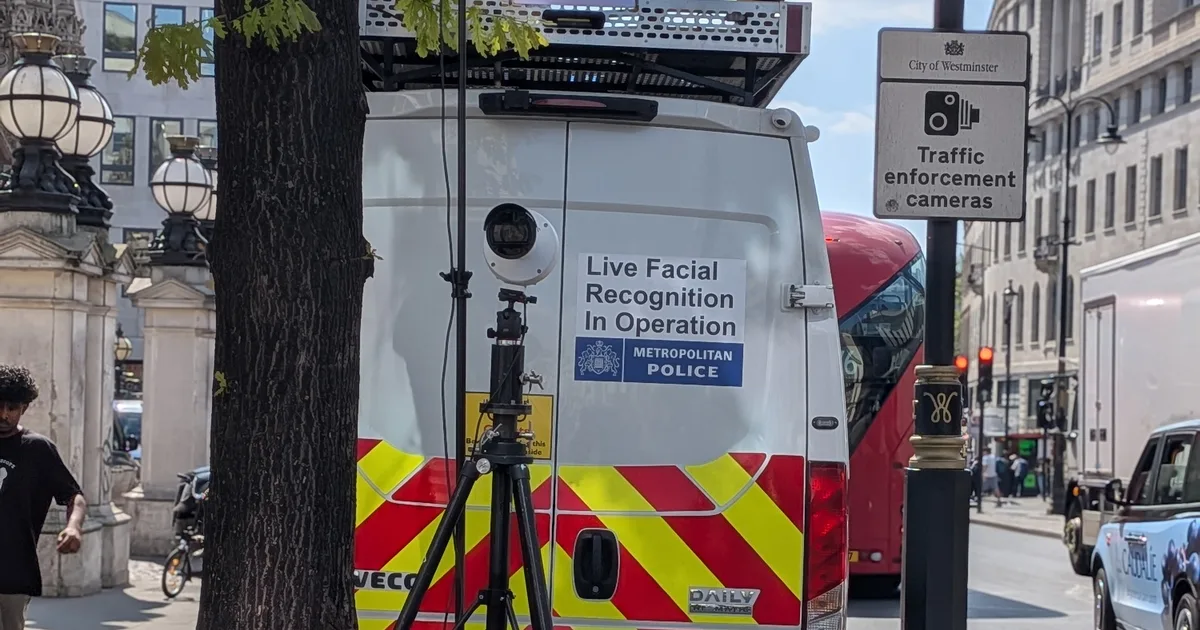 A Metropolitan Police van marked 'Live Facial Recognition In Operation' with a camera on a tripod beside it, parked on a London street next to a City of Westminster traffic enforcement camera sign.
