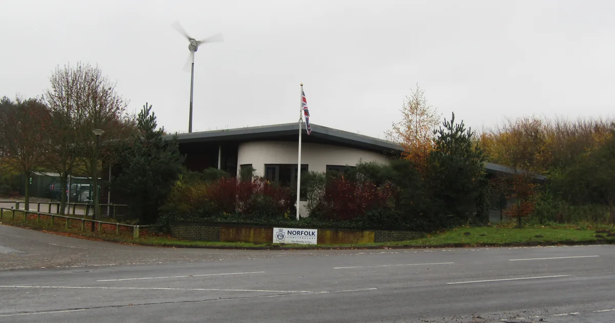 Norfolk Constabulary's police station on Holt Road in Cromer, a single-storey building with a Union flag, a small wind turbine and a Norfolk Constabulary sign at the entrance.