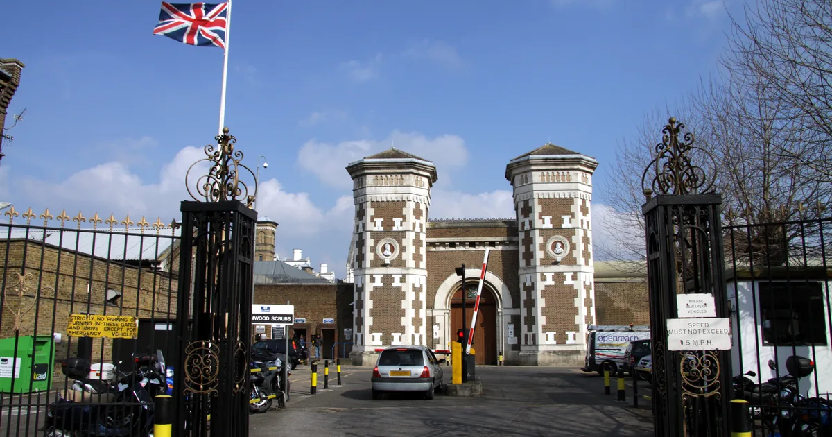 The Victorian gatehouse and entrance towers of HM Prison Wormwood Scrubs in London, seen from the road with the perimeter gates open.