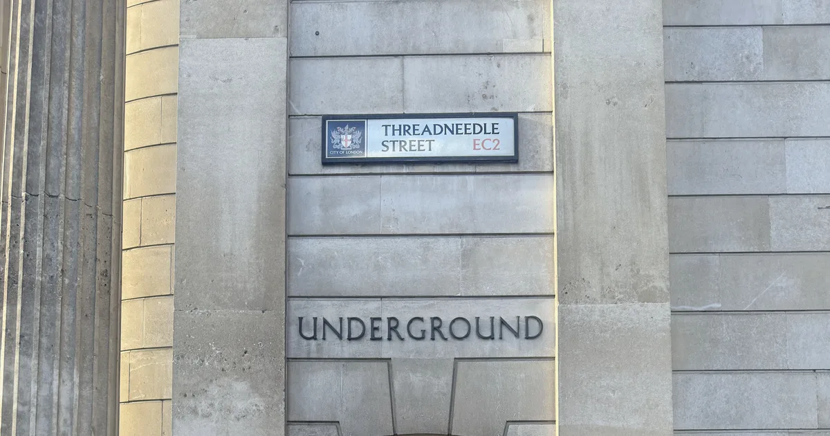 A street sign reading Threadneedle Street EC2 mounted on a stone building above an Underground station entrance in the City of London.