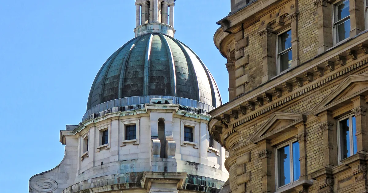 The copper dome and stone cupola of the Old Bailey, the Central Criminal Court in London, with part of an adjoining building to the right, against a clear sky.