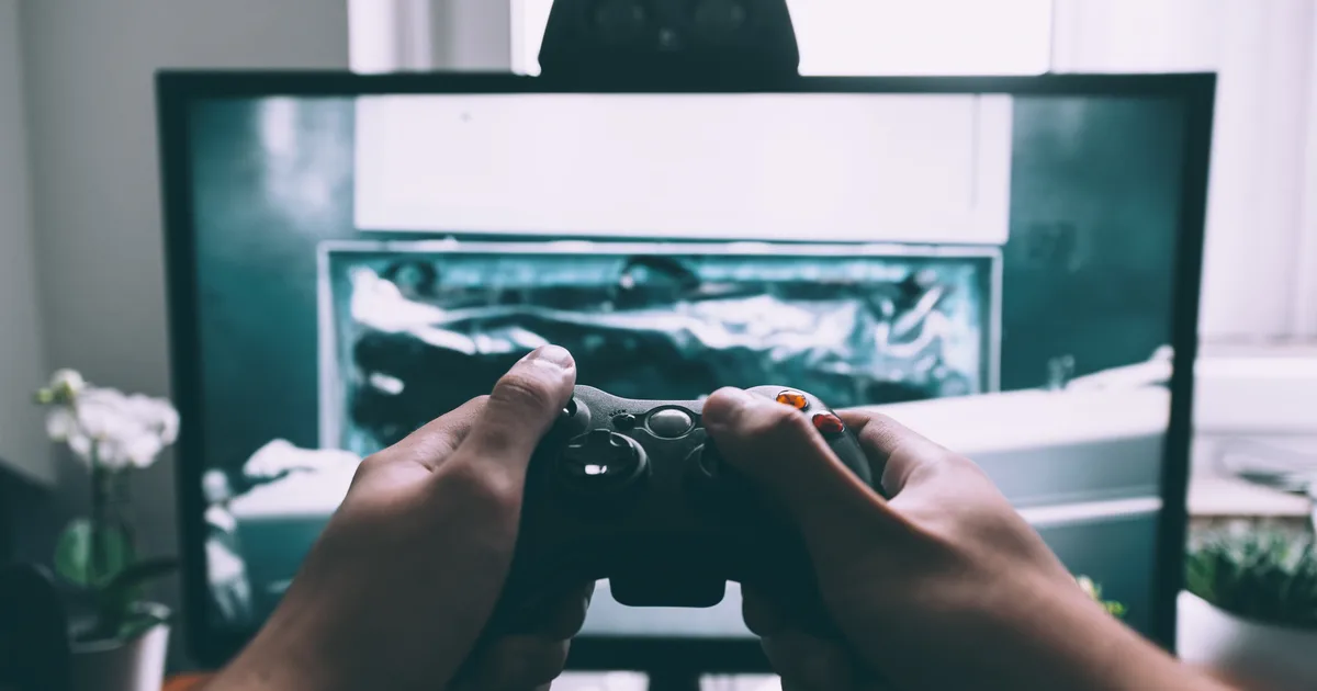 Close-up of two hands holding a video game controller in front of a television screen in a living room.
