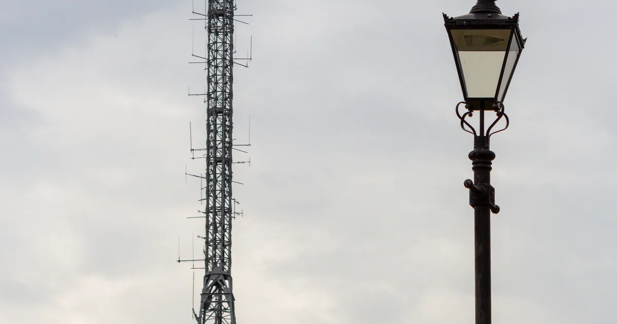 A television transmitter mast rising above trees at Alexandra Palace, London, with a Victorian lamp post in the foreground.
