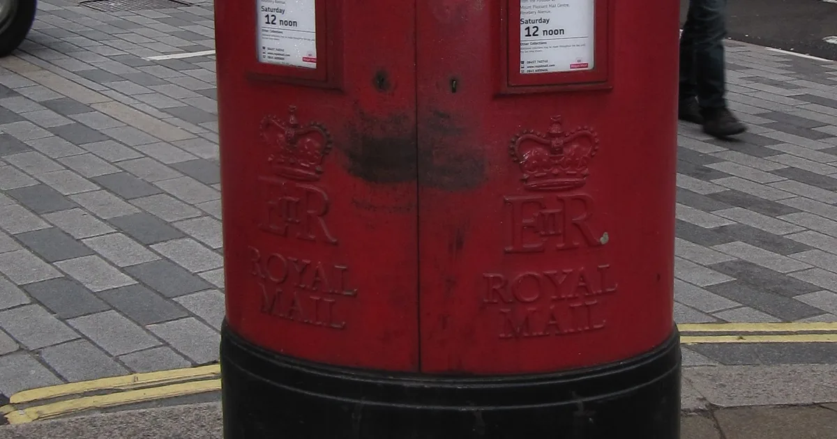 A red Royal Mail pillar box, close on the embossed crown and 'ROYAL MAIL' lettering.