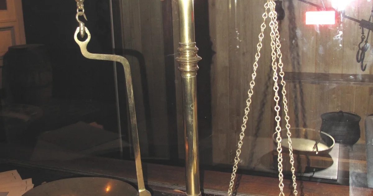 A set of brass equal-arm beam scales on a wooden stand, photographed against a plain background.