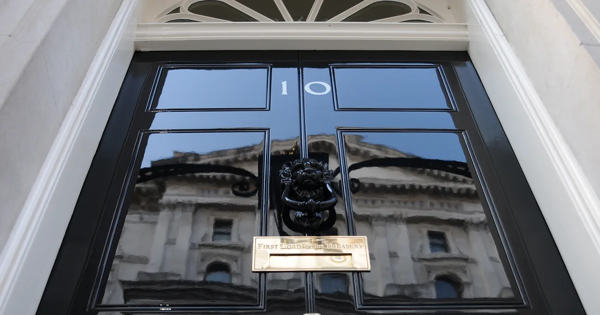 The famous black door of 10 Downing Street, London, photographed from below, showing the number 10 and the 'First Lord of the Treasury' nameplate beneath the lion's-head knocker.