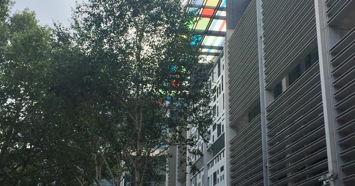 The Home Office headquarters at 2 Marsham Street, London, showing its perforated white cladding and coloured glass canopy above the entrance, seen through trees.