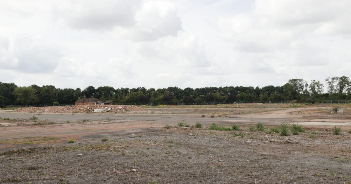 The cleared, derelict site of the former Kempston Hardwick brickworks, Bedfordshire, with demolition rubble and a tree line in the background.